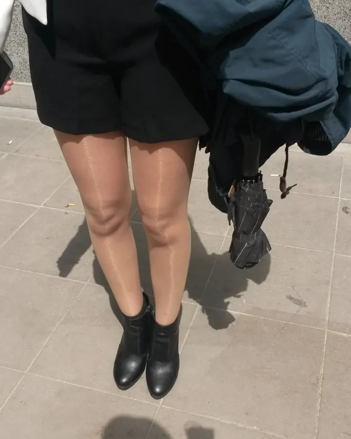 Femme aux cheveux noirs portant un haut noir et des collants à mailles, assise sur un fauteuil beige, tenant une canne.