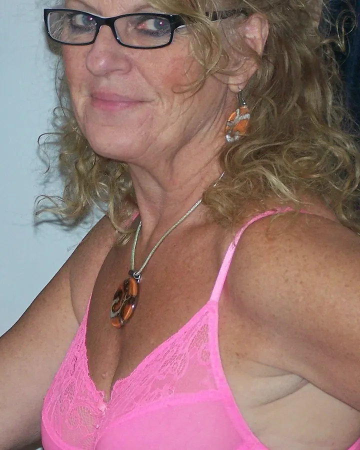 Femme aux cheveux blonds bouclés, en soutien-gorge rose fluo, portant des lunettes noires, regardant de côté.