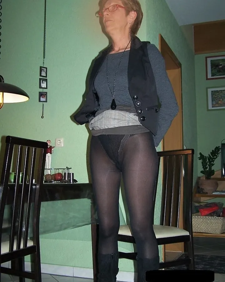Femme aux cheveux blonds courts, en robe noire à sequins, assise sur un canapé beige, souriant à la caméra.