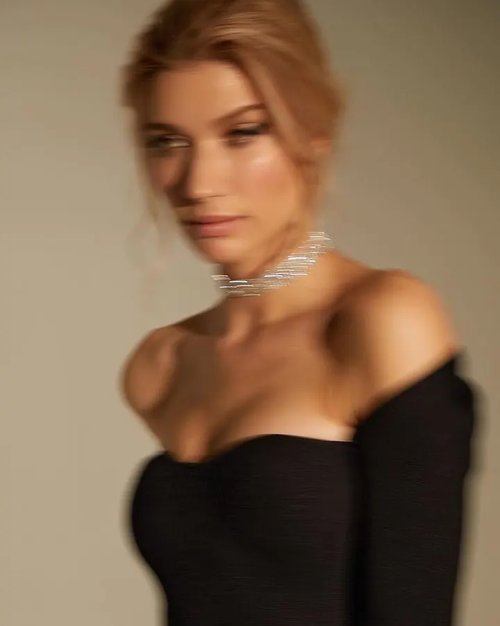 Femme blonde en robe noire décolletée, collier argenté, regard doux, lumière chaude