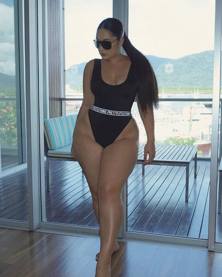Femme aux cheveux noirs en maillot de bain noir, lunettes de soleil, sur terrasse avec vue sur port