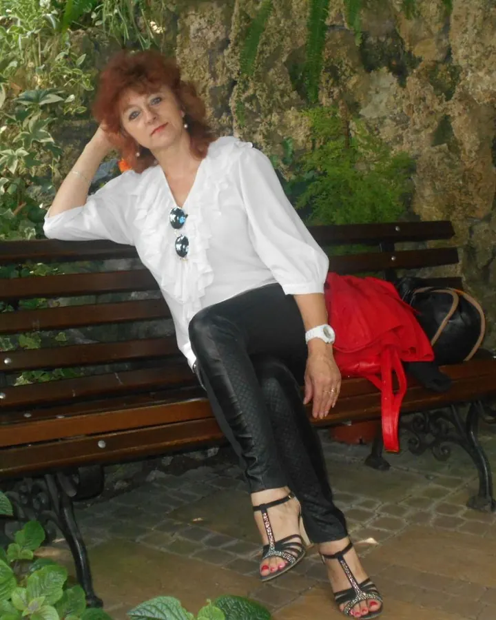 Femme en robe noire, assise sur un canapé, portant des collants noirs et des chaussures rouges.