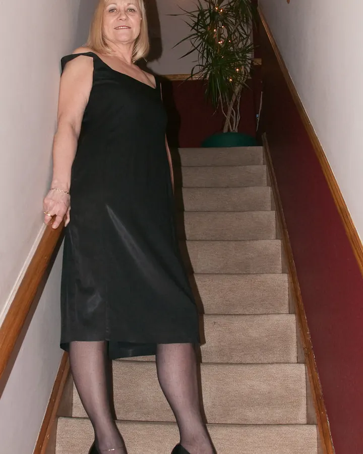 Femme aux cheveux blonds en robe blanche, assise sur un canapé, regardant l'appareil.