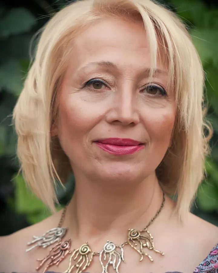 Femme aux cheveux bruns-noirs, regardant vers la caméra, souriant légèrement, dans un cadre neutre.