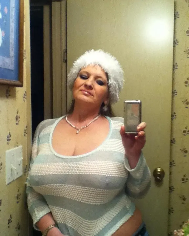 Femme en haut blanc, avec une casquette de fourrure blanche, prenant un selfie dans un miroir.